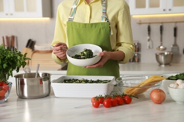 Woman making spinach lasagna at marble table in kitchen, closeup