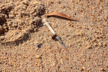 A plastic disposable syringe lies in the sand on the beach. Environmental pollution. A dangerous find on the beach