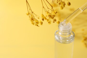 Dripping serum from pipette into bottle and gypsophila flowers on yellow background, closeup. Space...