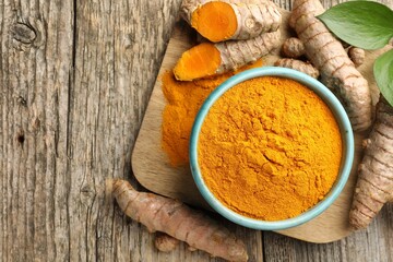 Turmeric powder in bowl, roots and leaves on wooden table, flat lay. Space for text