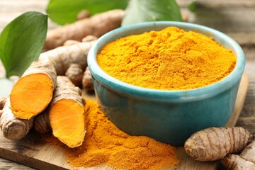 Turmeric powder in bowl, roots and leaves on table, closeup