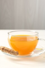 Aromatic turmeric tea in glass cup and root on white wooden table, closeup