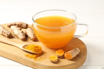 Aromatic turmeric tea in glass cup, roots and powder on white wooden table, closeup