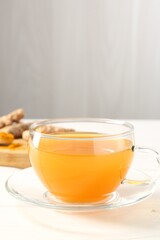 Aromatic turmeric tea in glass cup on white table, closeup