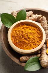 Aromatic turmeric powder in bowl, fresh roots and leaves on light grey table, closeup