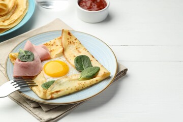Delicious crepes with egg, ham, basil and sauce on white wooden table, closeup. Space for text