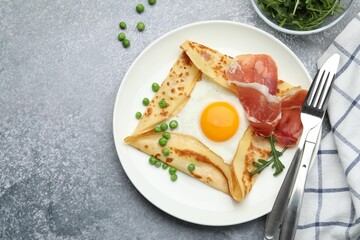 Delicious crepe with egg, bacon, arugula and green peas on grey table, flat lay. Space for text