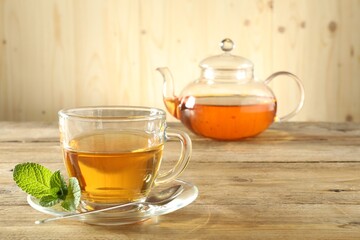 Freshly brewed tea in glass cup and teapot on wooden table