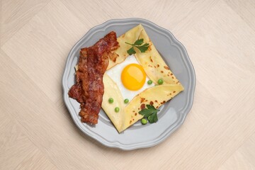 Delicious crepe with egg, bacon and green peas on wooden table, top view. Breton galette