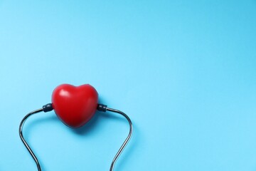 Stethoscope and red decorative heart on light blue background, top view. Space for text