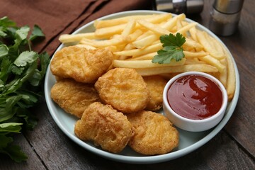 Tasty chicken nuggets and french fries with sauce on wooden table, closeup