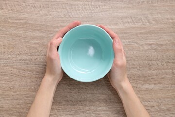 Woman holding empty bowl at wooden table, top view