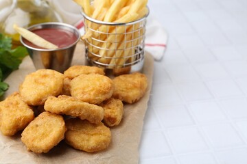 Tasty chicken nuggets, potato fries and ketchup on white tiled table, closeup. Space for text