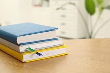 Stack of books with colorful bookmarks on wooden table, closeup. Space for text