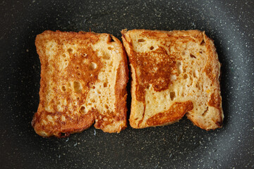 Close-up of two nicely golden pieces of French toast cooking in a skillet, making traditional breakfast