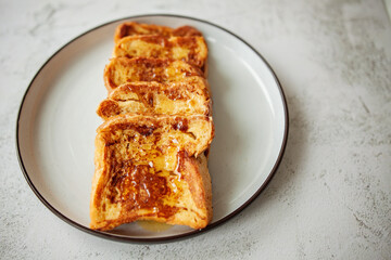 French toast with honey, traditional sweet homemade breakfast of bread soaked in eggs and milk, served on a white plate and shot in bright morning light with copy space on right side