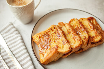Traditional homemade breakfast - a cup of coffee and French toast with honey,   bread soaked in eggs and milk, served on a white plate and shot in bright morning light with copy space on left side