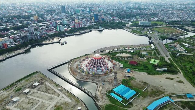 The atmosphere of the construction of Losari Beach and the 99-dome mosque with the backdrop of the cityscape on a sunny day and clear sea.