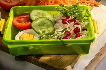 Lunch box with salads and vegetables. Fresh cabbage salad with cranberries. Half of boiled egg, tomato, fresh cucumber, microgreens.