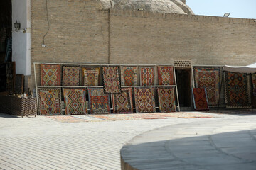 traditional Uzbek carpets are hung along the brick wall of a building, Bukhara