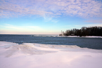 Small bay in Lake Ontario partially covered by ice with forest in the background