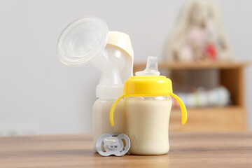 Feeding bottles with milk, breast pump and pacifier on wooden table indoors