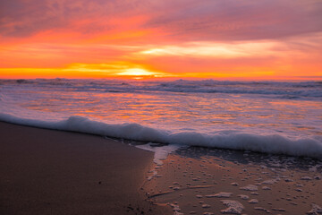Beautiful sunset on the ocean, sea foam shot close-up, with the setting sun and sky coloured by the sunset rays in the background