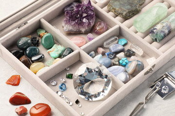 Box with beautiful gemstones and jeweler's tools on light table, closeup