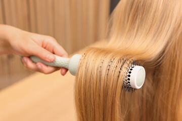 Fototapeta premium Hairdresser styling client's hair with round brush in salon, closeup