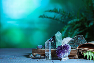 Beautiful natural gemstones and book on grey table against green background. Space for text