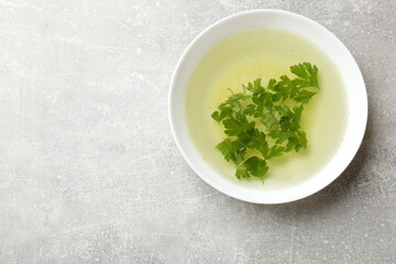 Tasty chicken bouillon with parsley in bowl on grey table, top view. Space for text