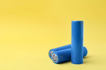 Three AA cell batteries on yellow background, closeup. Space for text