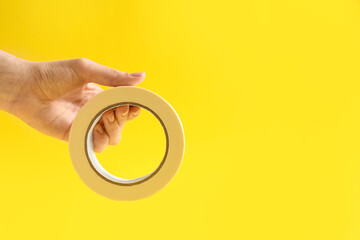Woman holding masking tape on yellow background, closeup. Space for text