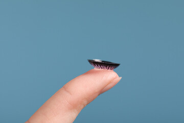 Woman with color contact lens on light blue background, closeup