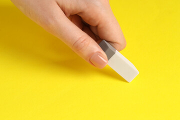 Woman using eraser on yellow background, closeup