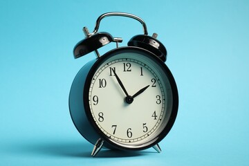 One black alarm clock on light blue background