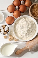 Rolling pin and ingredients for dough on white wooden table, flat lay
