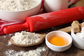 Rolling pin and ingredients for dough on wooden table, closeup