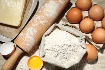 Rolling pin and different ingredients on light wooden table, flat lay