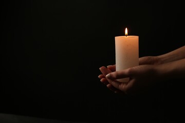 Woman with burning candle on dark background, closeup. Space for text