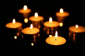 Many burning candles on dark background, closeup