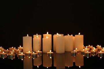 Many burning candles on mirror surface in darkness