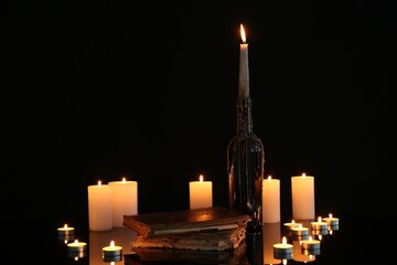 Many burning candles and books on mirror surface against black background