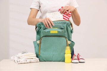 Mother packing baby's stuff into bag at white table, closeup