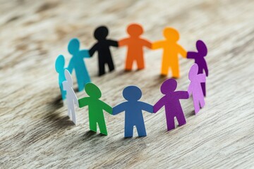 A circle of colorful paper cutout figures holding hands on a wooden surface, symbolizing diversity, unity, and inclusion