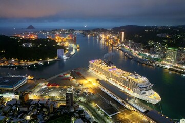 Panorama of beautiful Keelung City at dusk, a busy seaport in northern Taiwan, with view of a cruise liner parking in the harbor and buildings by the wharf in blue twilight