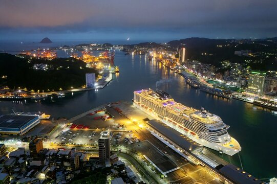Panorama of beautiful Keelung City at dusk, a busy seaport in northern Taiwan, with view of a cruise liner parking in the harbor and buildings by the wharf in blue twilight