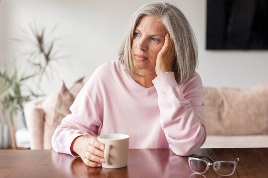Sad pensive middle age woman looking down depressed sitting on the sofa