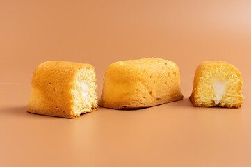 Two cakes, one cut in half on a brown background. The cake is yellow with white filling.