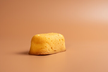 A small yellow cake on a brown background. It is not covered with icing. The cake is close-up.